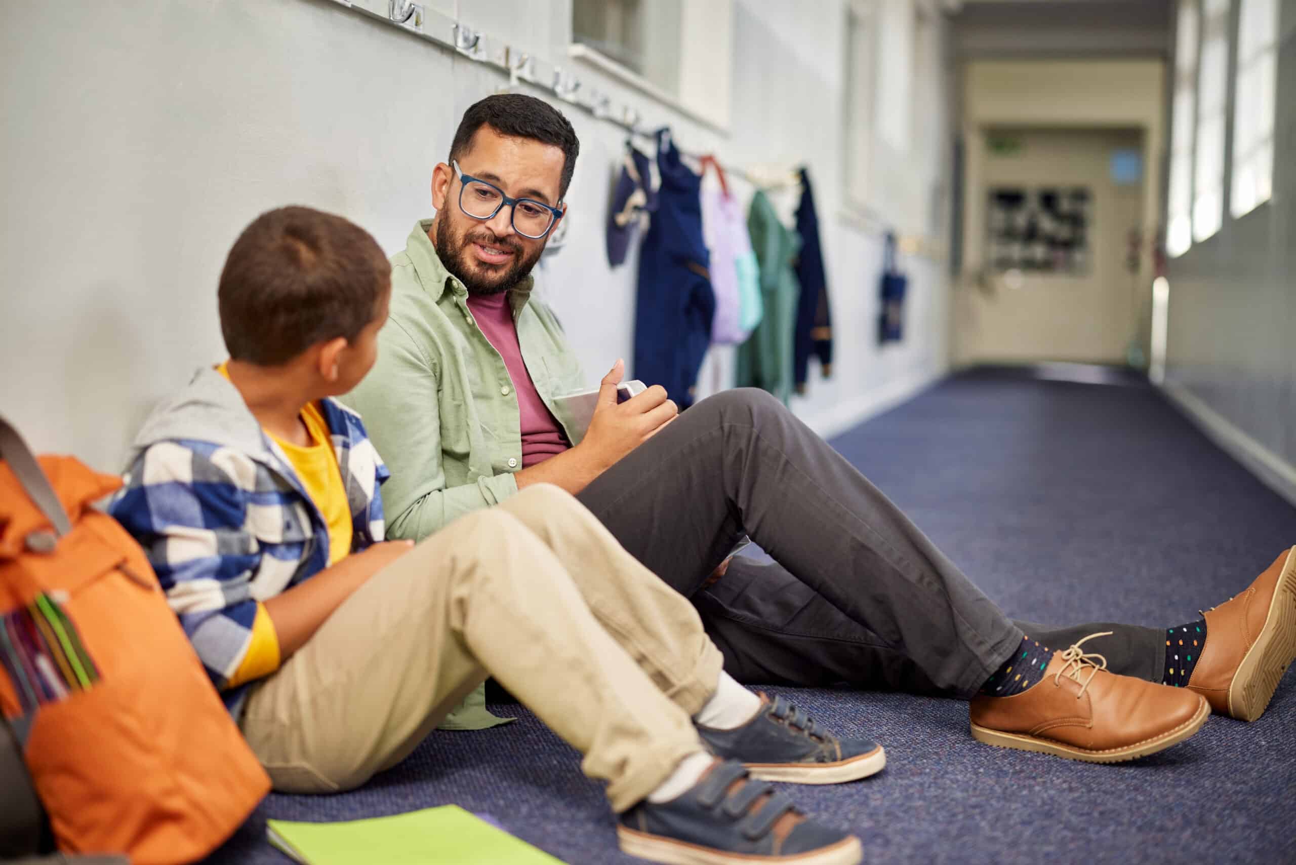 Young and friendly teacher speaking to a student in school hallway.